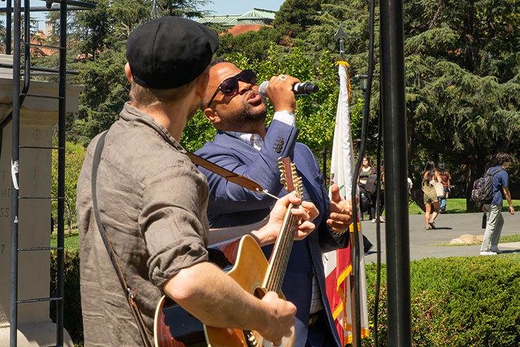 a man in a blue suit sings outside standing next to a guitar player