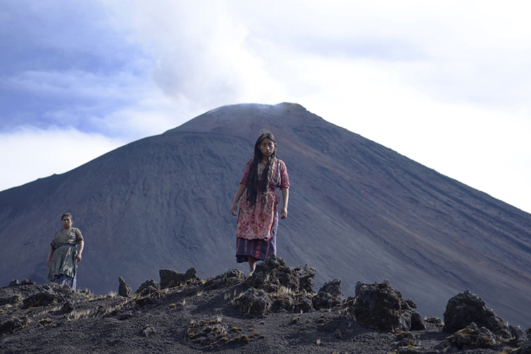 a girl stands on rocks in front of a volcano