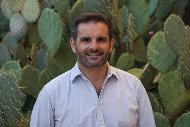 Laureano (Lau) Gherardi smiles at the camera standing in front of cacti