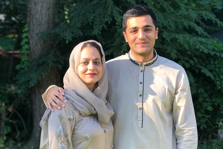 a son has his arm around his mom's shoulders standing outside and smiling