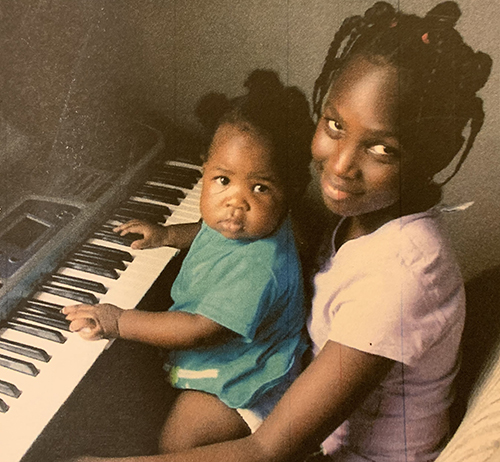 Daniella as a baby sits on her older sister's lap and plays a keyboard.