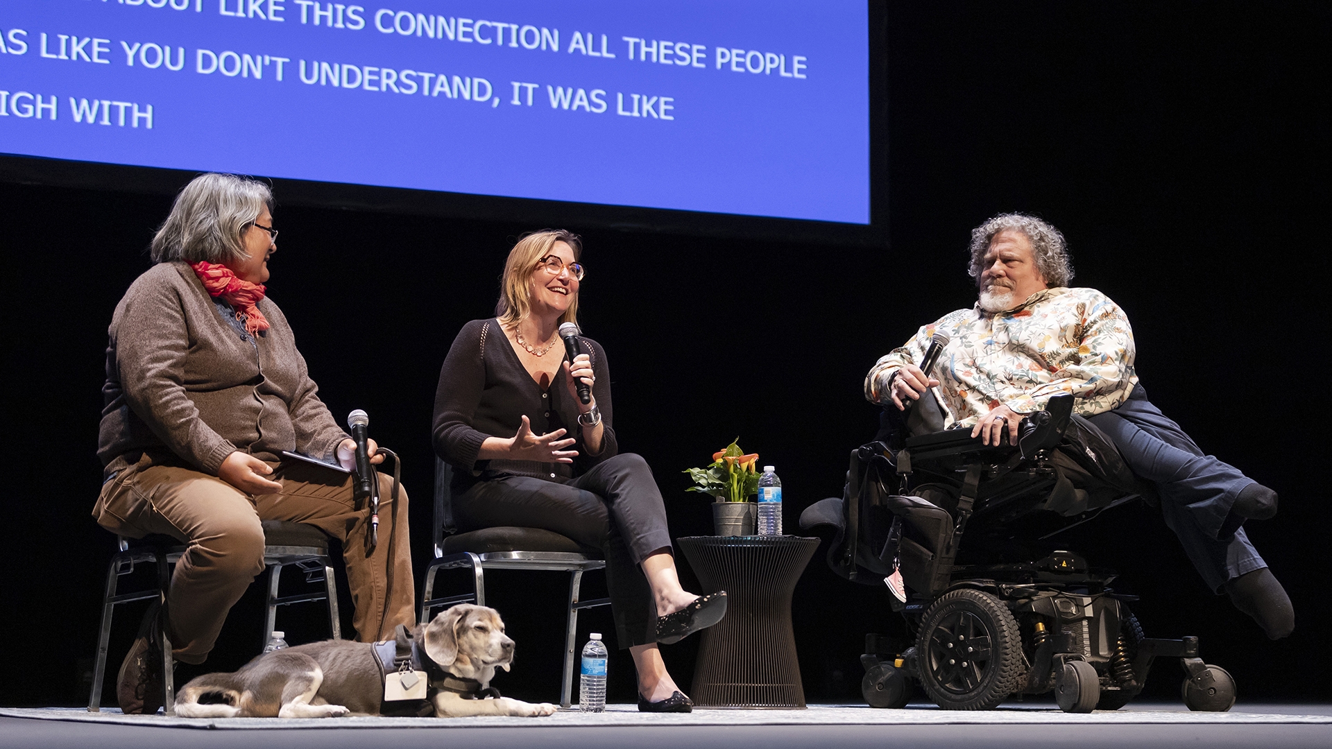 three people sit on stage with microphones talking to an audience