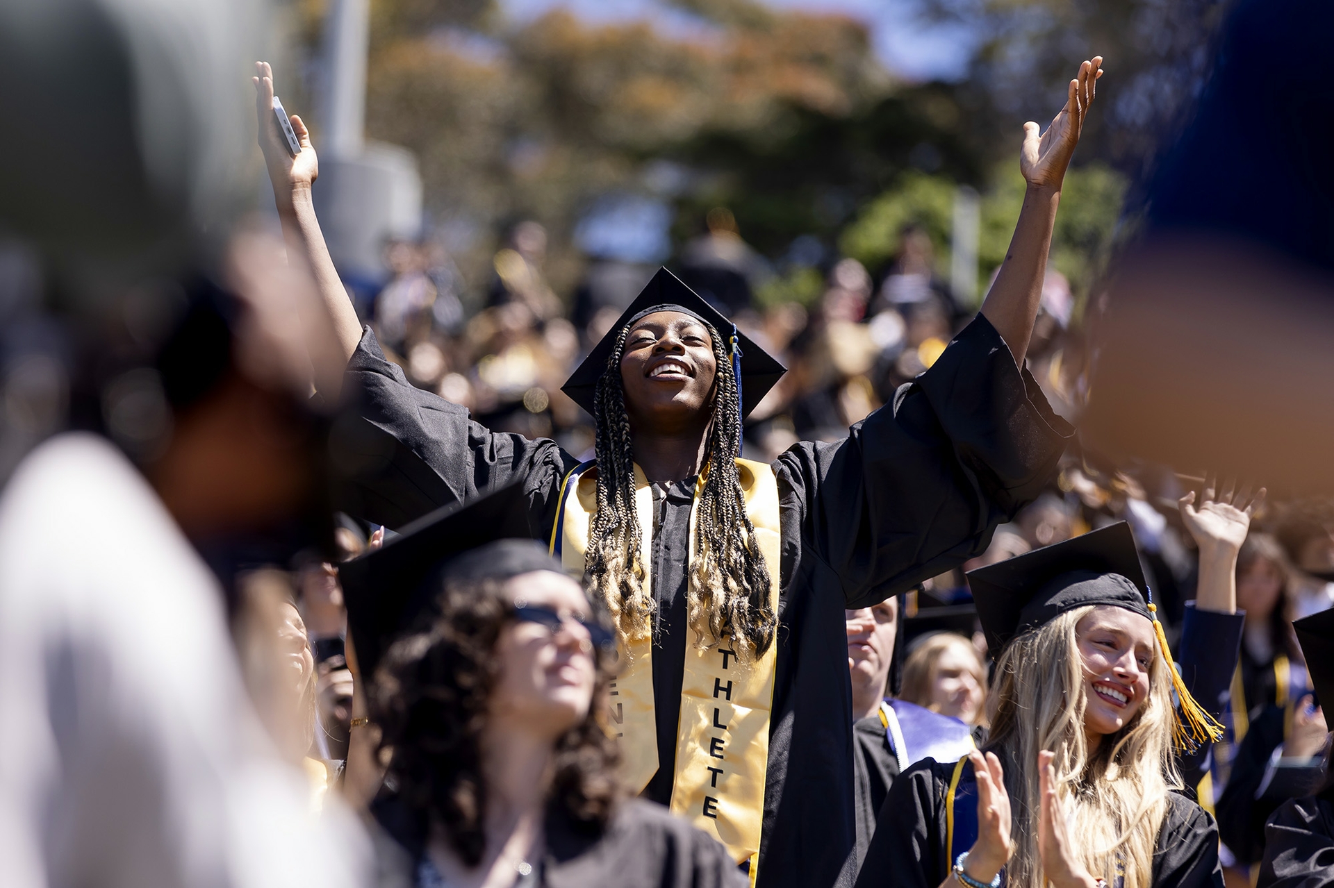 A young man in commencement robes with hands raised in joy